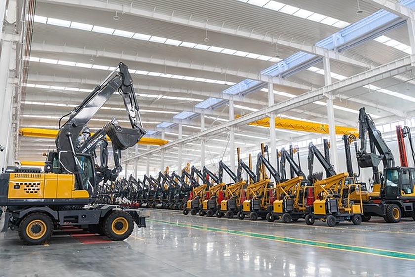 Line of mini excavators in a bright assembly hall with an overhead crane